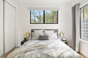 Ein Schlafzimmer mit einem Bett, zwei Nachttischen, einem Fenster mit Blick auf Bäume und einem Vorhang.