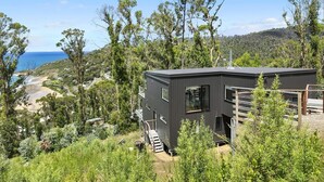 A modern building with a dark exterior, surrounded by greenery and overlooking a beach. - Vue Sur La Mer (Wye River)