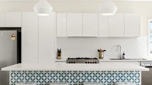 A modern kitchen with white cabinets, a central island with bar stools, a gas stove, and pendant lighting. - Vue Sur La Mer (Wye River)