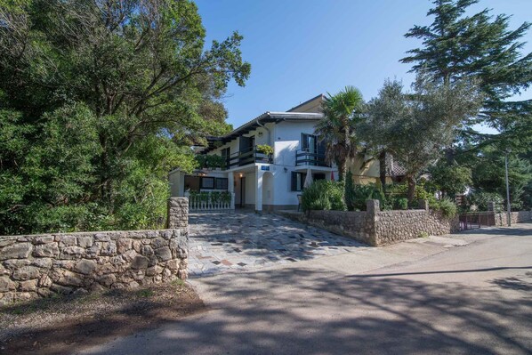 A two-story house with a stone wall entrance, a balcony, and a paved driveway.
