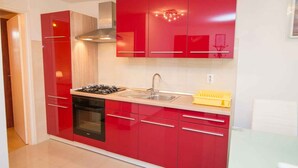 A modern kitchen with red cabinets, a gas stove, a sink, and a yellow dish rack. - Holiday apartment only 150 m from the sea (Artatore)