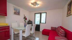 A modern living room with a glass dining table, white chairs, a red sofa, and a television. - Holiday apartment only 150 m from the sea (Artatore)