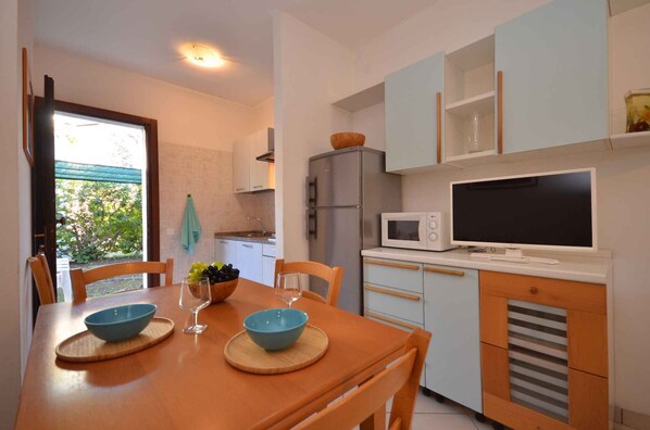 A compact kitchen with a dining table, chairs, a microwave, a refrigerator, and a television.
