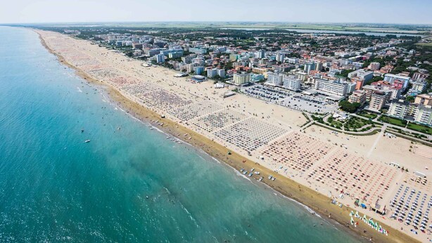Luftaufnahme einer Küstenstadt mit einem langen Strand, zahlreichen Gebäuden und einem klaren Himmel.