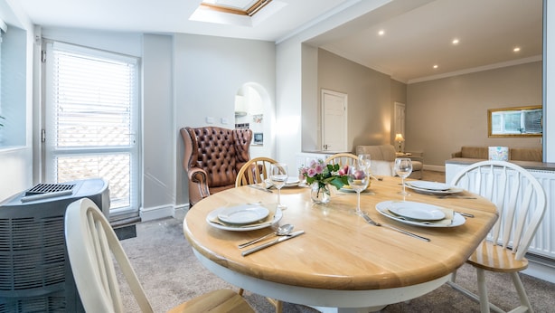 Comedor con una mesa de madera redonda dispuesta para cuatro personas, rodeado de sillas blancas.