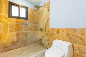 A bathroom with a shower, a toilet, and a window.