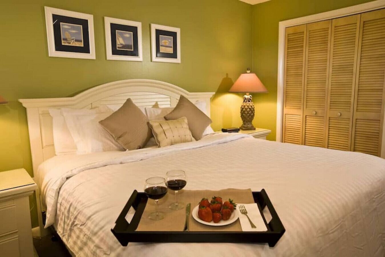 A neatly made bed with a tray of strawberries and wine glasses on it.