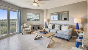A spacious living room with a large window, a ceiling fan, a sofa set, a coffee table, and a fireplace. - Dazzling Ocean View Suite w/heated pool, beach, marina, tennis/pickleball (Tavernier)