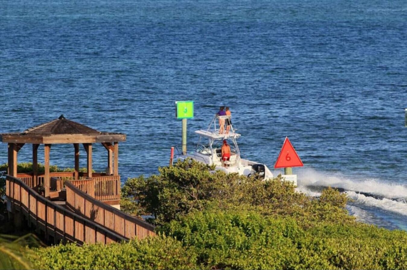 A wooden gazebo overlooking a body of water, a small boat with a person on it, and a red triangular sign with the number 6.