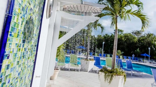 A pool area with a palm tree, a showerhead, and blue lounge chairs. - Dazzling Ocean View Suite w/heated pool, beach, marina, tennis/pickleball (Tavernier)