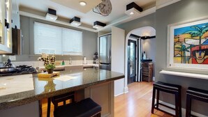 A modern kitchen with a granite countertop, stainless steel appliances, and a clock on the wall. There is a window with blinds, a door leading to another room, and a painting on the wall. - Lower Suite: a classic suite in a quiet Seattle home (Seattle)