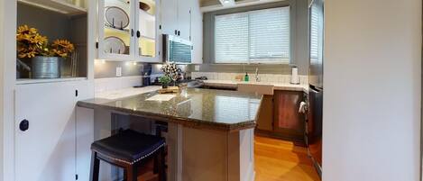 A modern kitchen with a granite countertop, white cabinetry, and a built-in island with bar stools.