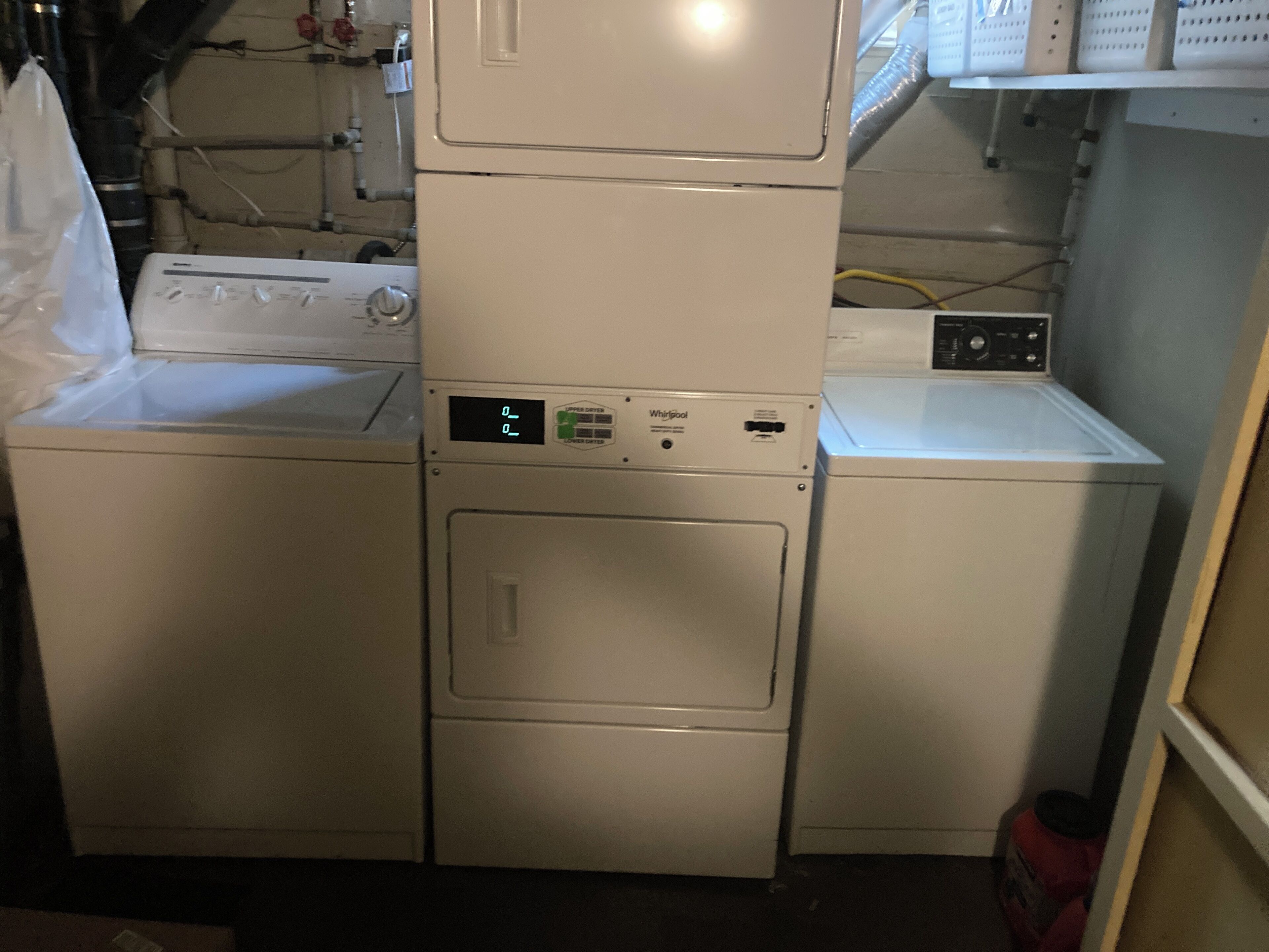 A laundry room with stacked washers and dryers, a visible control panel, and a hose reel on the wall.
