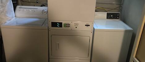 A laundry room with stacked washers and dryers, a visible control panel, and a hose reel on the wall.