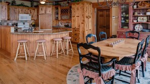 A wooden kitchen with a central island, bar stools, a dining table with chairs, and a chandelier.