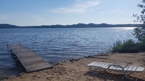 A beach with a wooden pier extending into calm waters, a sandy shore, and a white lounge chair.