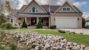 A two-story house with a garage, a front porch, and a stone retaining wall.