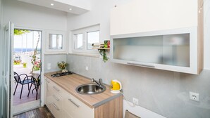 A modern kitchen with a sink, stove, and a yellow kettle. There is a window with a view of the city. - Rooms Rita - Double Room with Private Bathroom (No. 2) (Dubrovnik)
