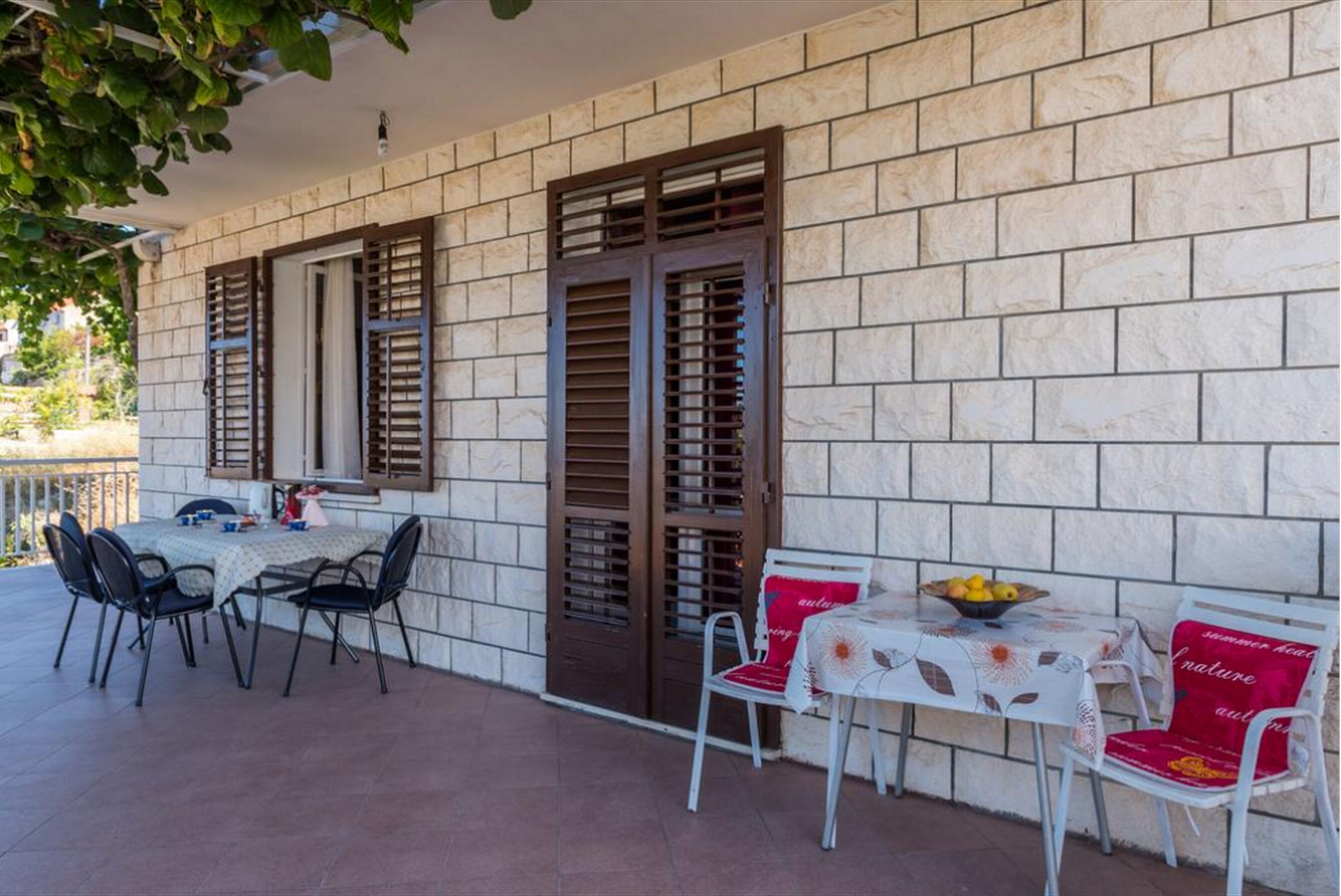 Um pátio externo com mesa e cadeiras, uma porta com persianas e vista para uma área residencial.