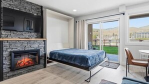 Een slaapkamer met een stenen openhaard, een bed, een stoel en uitzicht op een grasveld door een schuifdeur.