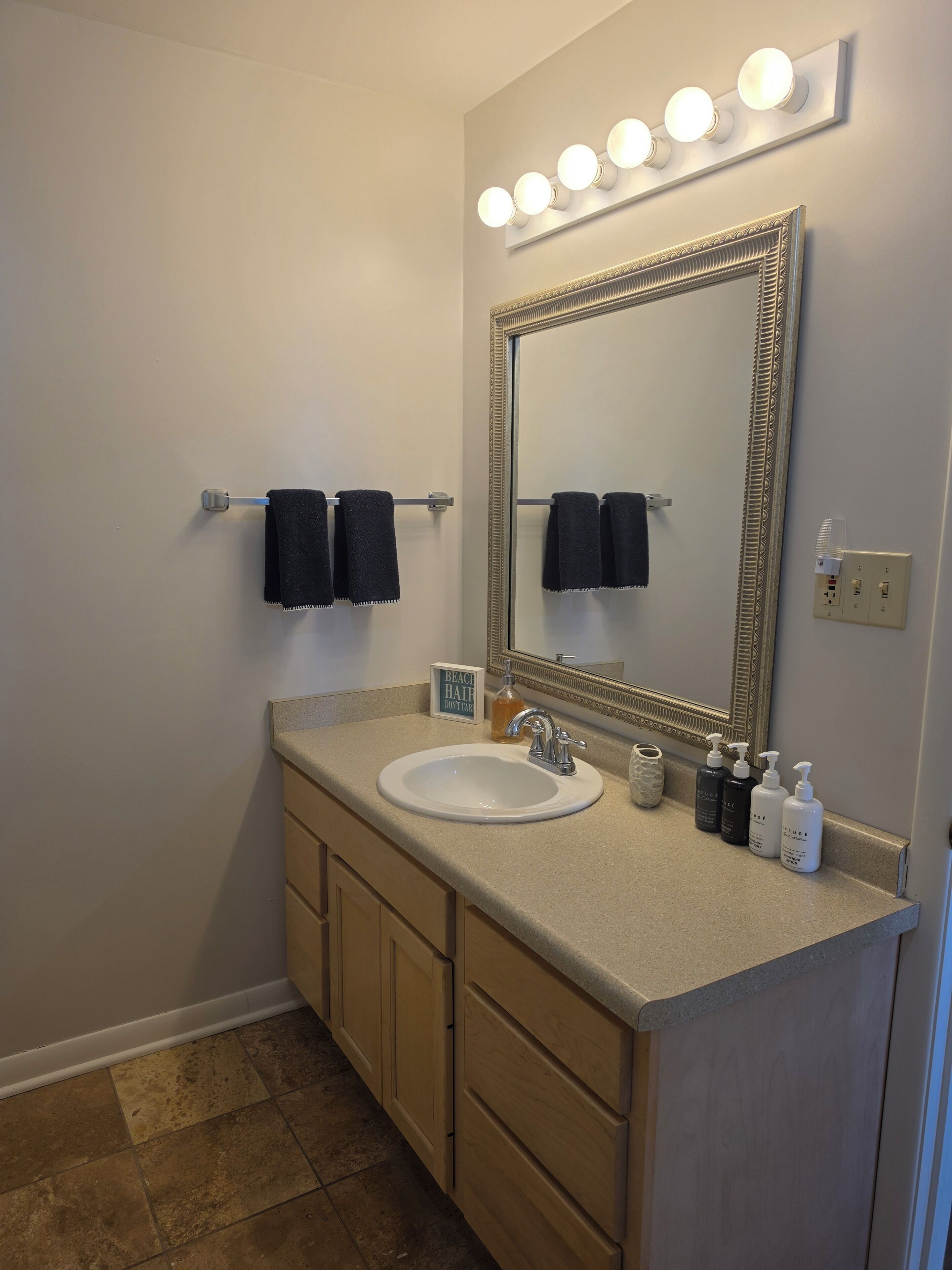 Une salle de bain équipée d’un lavabo, d’un miroir, d’un porte-serviettes et d’articles de toilette.