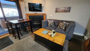 Een woonkamer met een bank, salontafel, televisie, open haard en een eethoek met stoelen en een tafel.