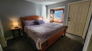 Een slaapkamer met een houten bed, nachtkastje met lamp, een raam met blinds en een deur.