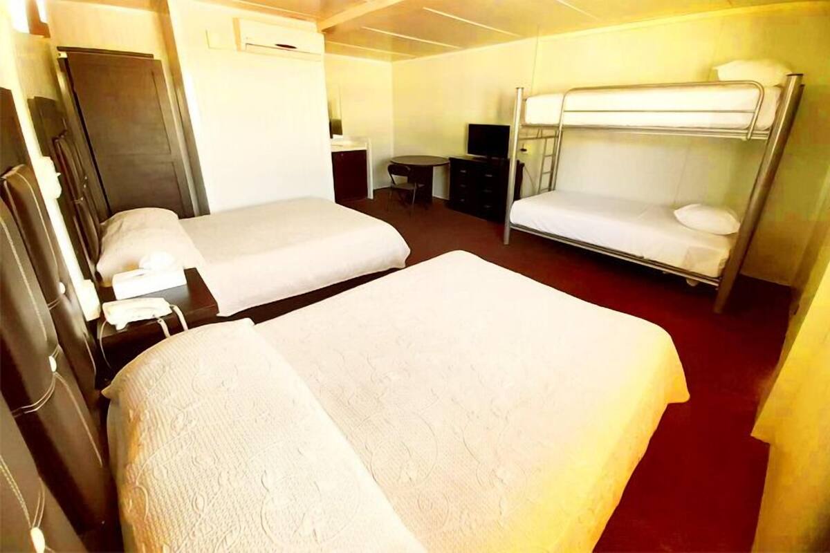 A hotel room with two single beds, a desk with a chair, a television, and a wardrobe.
