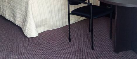 Et hotelværelse med seng, stol, skrivebord og telefon.