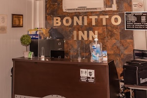 Un comptoir d'accueil à l'hôtel Bonitto Inn, avec un panneau indiquant les tarifs des chambres et les services proposés.