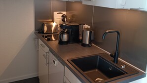 Ett kompakt kök med inbyggd diskmaskin, kaffebryggare och vattenkokare.