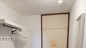 En smal hall med en dörr, en klädhängare och en säng.