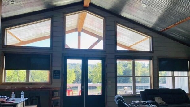 A spacious room with a high ceiling, large windows, a wooden ceiling, and a couch. - Livin on the Edge on the Caddo River (Glenwood)