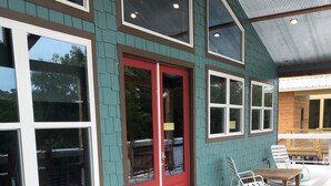 A covered patio with a table and chairs, a red door, and a view of the backyard. - Livin on the Edge on the Caddo River (Glenwood)
