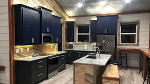 A modern kitchen with dark cabinets, a central island, and a stainless steel refrigerator. - Livin on the Edge on the Caddo River (Glenwood)