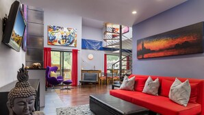 A modern living room with a red sofa, a Buddha statue, a flat-screen TV, and a large painting. - Vail21 601 - 3 Bedroom Gold (Vail)
