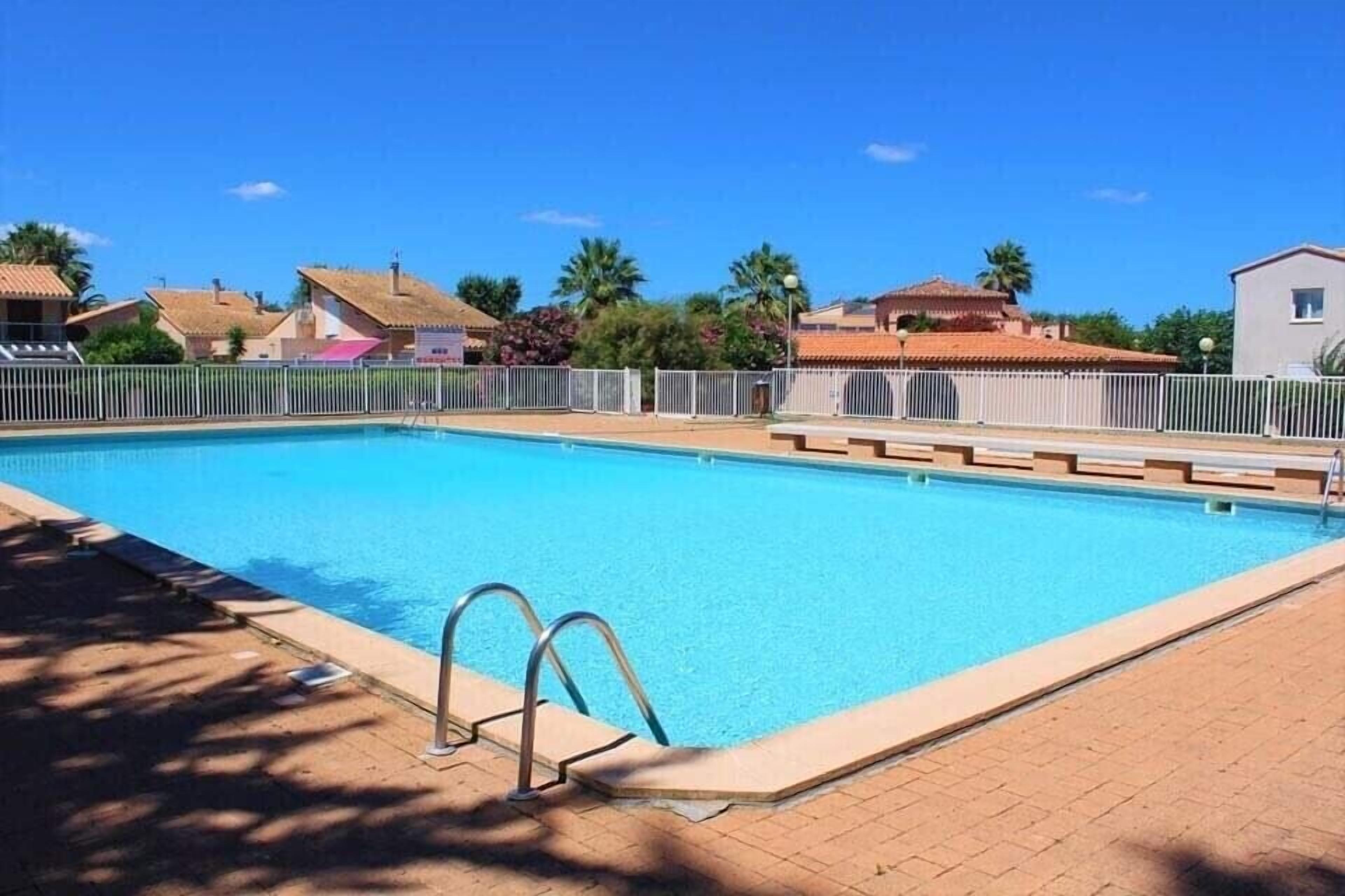 Una piscina cristalina con una cerca blanca, rodeada de casas y palmeras.
