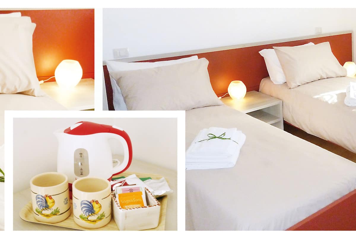 Une chambre d’hôtel avec deux lits, une table de chevet avec une lampe et une petite table avec une bouilloire, des tasses et un plateau de nourriture.