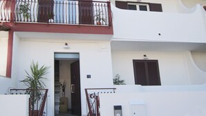 Un edificio residencial de dos plantas con un balcón, una puerta y un ventanal pequeño.