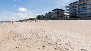 Una playa con una hilera de edificios de varios pisos, arena y cielo despejado.