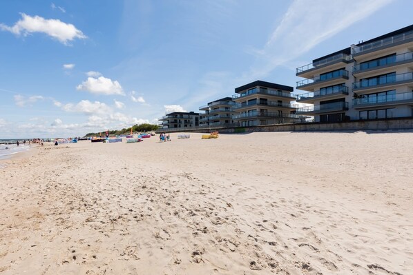 Una playa con una hilera de edificios de varios pisos, arena y cielo despejado.