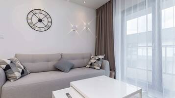 Ein modernes Wohnzimmer mit einer Couch, einem Couchtisch, einer Wanduhr und einem Fenster mit Vorhängen.