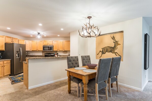 A modern kitchen with wooden cabinets, a stainless steel refrigerator, a microwave, and a dining area with a wooden table and chairs. - On Free Shuttle Route! Hot tub! Garage Parking! (Steamboat Springs)