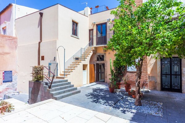 A courtyard with a staircase leading to a second-floor balcony, surrounded by buildings with balconies and potted plants. - Located in the ancient Corte dei Bottai, a few steps from Piazza del Duomo, this modern apartment is located in the heart of Ortigia, amidst architectural wonders and typical restaurants. The courtyard on which it stands is recently renovated and takes o (Siracusa)