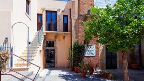 Um edifício com uma escadaria que leva a uma porta, plantas em vasos e uma árvore em primeiro plano.