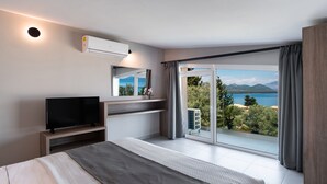 Un dormitorio moderno con una cama grande, televisor, aire acondicionado integrado y un balcón con vistas panorámicas.