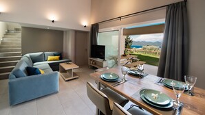 Una sala de estar moderna con un sofá, una mesa de comedor para dos personas y un ventanal con vistas al exterior.