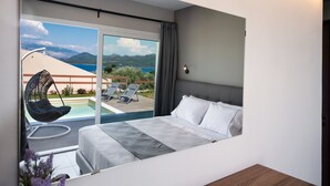 Una habitación de hotel moderna con una cama grande, vistas a la piscina y montañas, y un balcón con sillones de descanso.