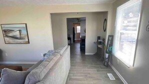 A living room with a grey sofa, a painting of a boat, and a hallway leading to a kitchen. - Fun getaway house with arcade. Cedar Point/Kalahari/Sports Force Park/Summit Rac (Norwalk)