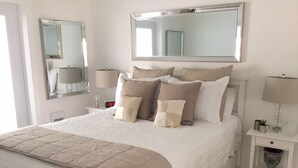 A neatly made bed with a beige quilt, a bedside table with a lamp, and a mirror above the bed. - One bedroom fully equipped Mahone Bay luxury cottage (Mahone Bay)